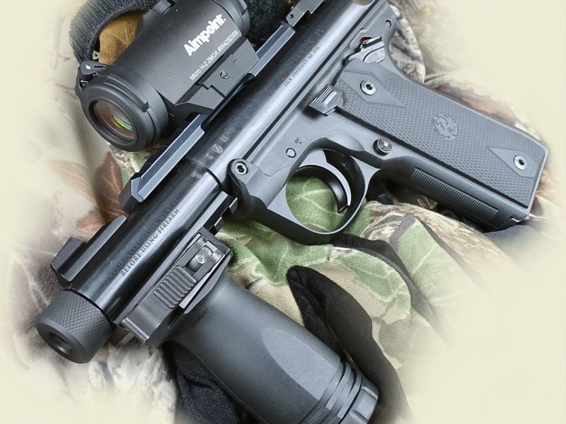 Celkový předoboční pohled na Ruger Mark IV Tactical. Jako doplnění standardních mechanických mířidel byla zbraň osazena elektrooptickým zaměřovačem Aimpoint Micro H-2 a na spodní taktické drážce je pak nasazena přídavná podpěrná rukojeť.