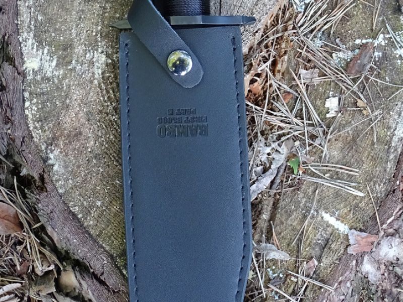 Dvojí boční pohled na nůž RAMBO FIRST BLOOD PART II. Jednak bez pouzdra a jednak zasunut ve svém černém pouzdře. I u dvojky je replika pouzdra vyrobena z umělé kůže. I zde ve slušné kvalitě, ale obdobně jako u jedničky i zde chybí kapsa na brousek.