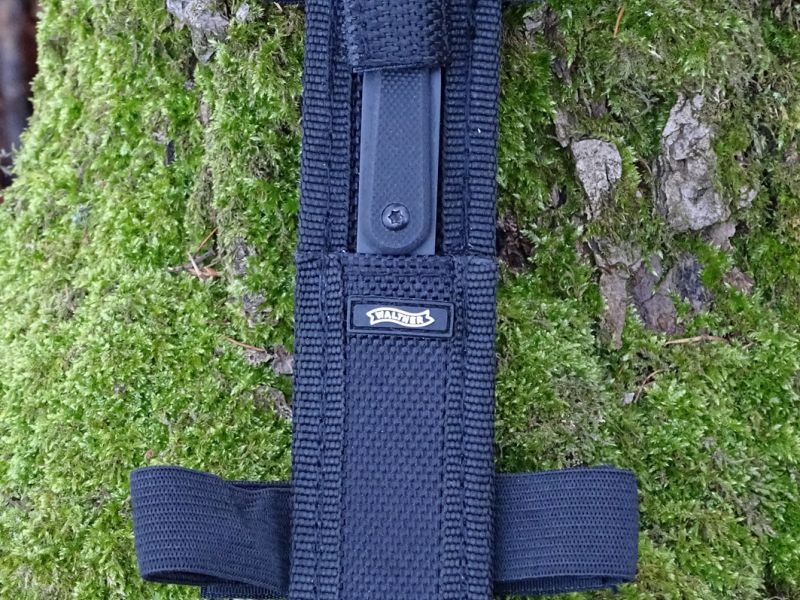 Nůž je dodáván s pouzdrem ze syntetických materiálů, které lze díky dvojici pružných širokých popruhů uchytit na předloktí ruky a zakrýt rukávem košile, mikiny nebo bundy.