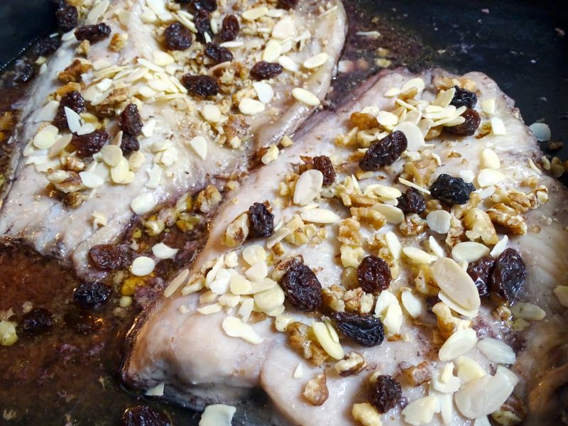 Po přibližně 45 minutách půlky kapra posypeme rozdrcenými vlašskými ořechy, sušenými rozinkami a kouskama mandlí. Opět podlejeme a dále pečeme.