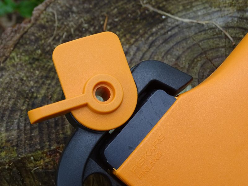 Zmíněný mechanický zámek drží sekerku v praktickém pouzdře. Díky tomu z pouzdra nevypadne a neumaže nebo nepoškodí své okolí. Samotný zámek je vlastně otočná plastová páka, jejíž funkce je dobře patrná z přiložených fotek. Nahoře je zámek uzamčen, dole pak umožňuje vyjmutí sekerky z pouzdra. Pouzdro je opravdu praktické, avšak by mohlo mít větší otvor pro prsty ruky. Větší ruka se silnějšími prsty se do oka již nevejde.