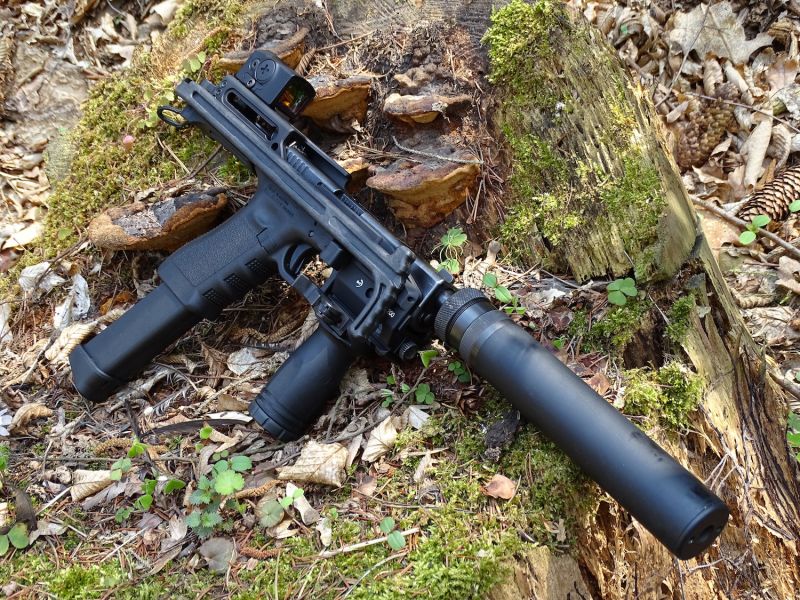 Pěkný pohled na pravou stranu konverze s pistolí Glock 17 se sklopenou ramenní opěrou, prodlouženým velkokapacitním zásobníkem, zaměřovačem Aimpoint ACRO, taktickou přední pistolovou rukojetí a tlumičem zvuku od stejného výrobce jako konverze.