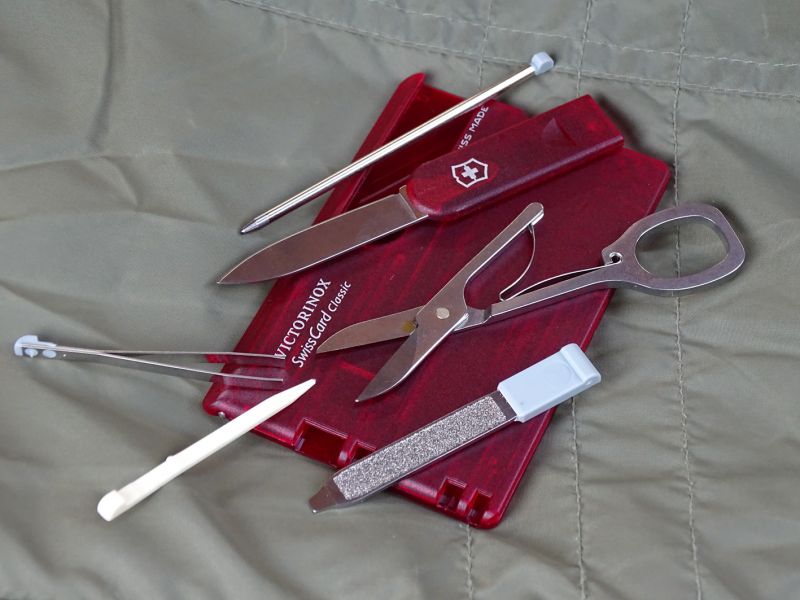 Kompletně „vysunutá“ karta Classic, tedy opět kromě špendlíku. Ten si prohlédněte na samostatných detailech. Shora kuličkové pero, pod ním ostrý malý nožík. Dále plně funkční nůžky a pilníček na nehty kombinovaný s plochým šroubováčkem 2,5 mm. Více vlevo pak nerezová pinzeta a plastové párátko.